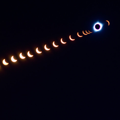 a combination shot showing the different phases of a solar eclipse against a black background. The sun in totality is near the upper left corner