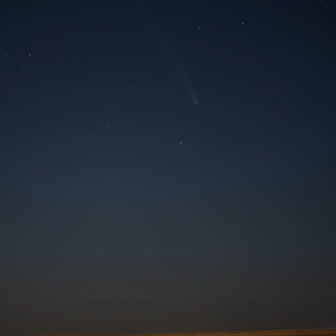 a faint comet with its head and tail against a dark sky sprinkled with stars